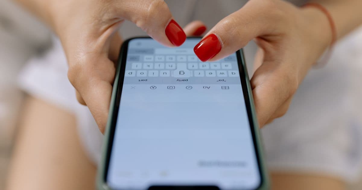 Mani con smalto rosso che scrivono un messaggio su uno smartphone